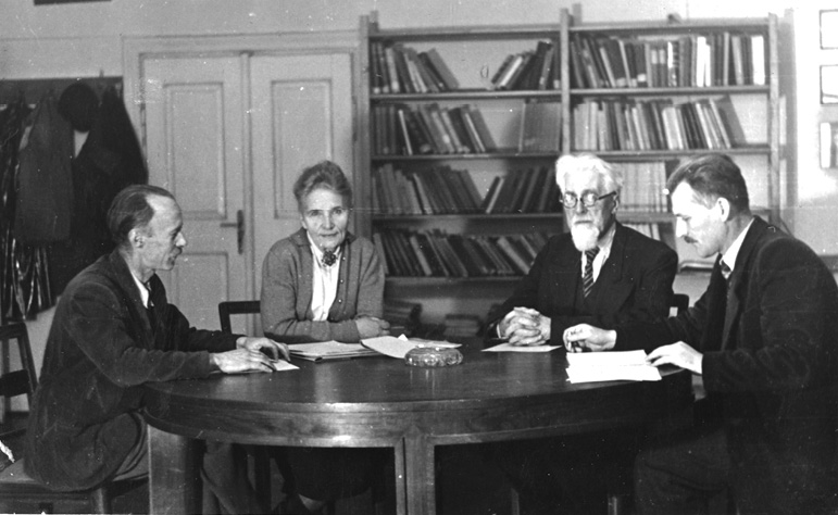A 1959 photograph taken in Professor Kazimierz Stołyhwo’s office at the Department of Anthropology, Jagiellonian University, Kraków. Four people sit in a row from left to right: Bronisław Jasicki, Eugenia Stołyhwo, Kazimierz Stołyhwo, and Paweł Sikora.