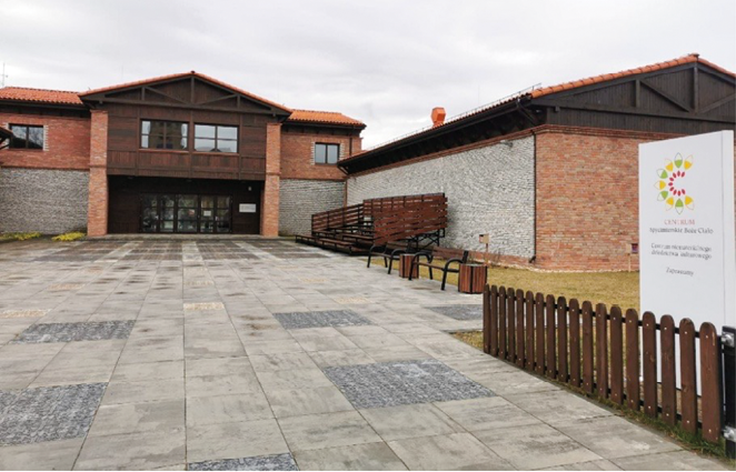 Widok od strony dziedzińca na trzyskrzydłowy kompleks Centrum „Spycimierskie Boże Ciało” w kształcie litery U, z kamienno-ceglanymi elewacjami i ceramicznymi dachami