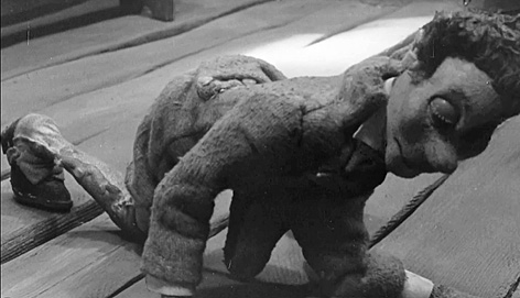 Czarno-biały kadr przedstawia postać Gawła na drewnianej podłodze. Gaweł ma zamknięte oczy, jest na czworakach.