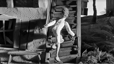 Postać Gawła odwrócona tyłem do widza zaczyna wchodzić po schodach. Schody mają układ pionowy. Lalka ubrana jest w białą koszulę, na stopach ma kapcie.