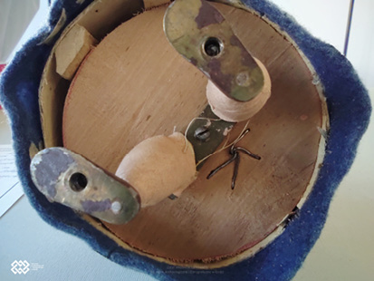 Widoczne jest łączenie nóg lalki gospodyni ze sklejką drewnianą za pomocą metalowych elementów.