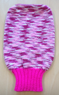 A hand-knitted uterus by Sue Tully, made with pink and white yarn, featuring a ribbed bright pink base. The soft textile sculpture lies on a wooden surface, showcasing detailed craftsmanship and anatomical form.