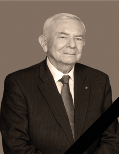 Portret Profesora doktora habilitowanego Jerzego Małeckiego w ciemnym garniturze i krawacie, wykonany w tonacji sepii. W prawym dolnym rogu zdjęcia umieszczono czarną żałobną wstęgę.