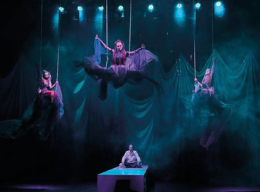 Scene 5, Act 3. The Witches talk to Hecate standing on the balcony while Macbeth is sleeping. The Witches (Anastasiia Ivahnenko – on the left, Anna Nimaiier – in the middle, Iryna Zhara – on the right) on the swings and Macbeth (Yakiv Kucherevskyi) sitting on a platform. Photo by Andrii Shepel.