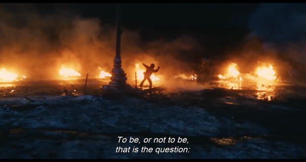 A man is standing in front of a fire. To be, or not to be, that is the question.