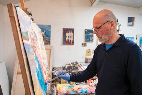 Zdjęcie z przyjaznej wobec wieku biblioteki obrazów przedstawiające starszego mężczyznę stojącego przy sztalugach i malującego obraz.