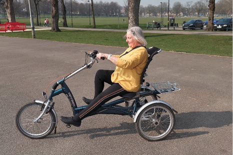 Zdjęcie z przyjaznej wobec wieku biblioteki obrazów przedstawiające starszą, siwowłosą kobietę zażywającą ruchu na stylowym trójkołowym rowerze dla dorosłych.