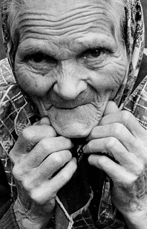 Czarno-biały portret starej kobiety w bliskim zbliżeniu, zamknięty w ciasnym kadrze. Kobieta patrzy prosto w obiektyw.