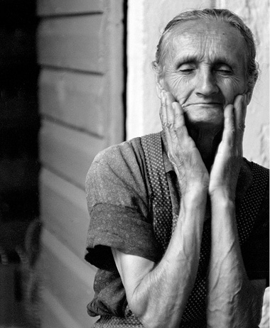 Czarno-biały porter starszej kobiety trzymającej głowę w dłoniach. Kobieta ma zamknięte oczy i jest spokojna, wyciszona, zamyślona.