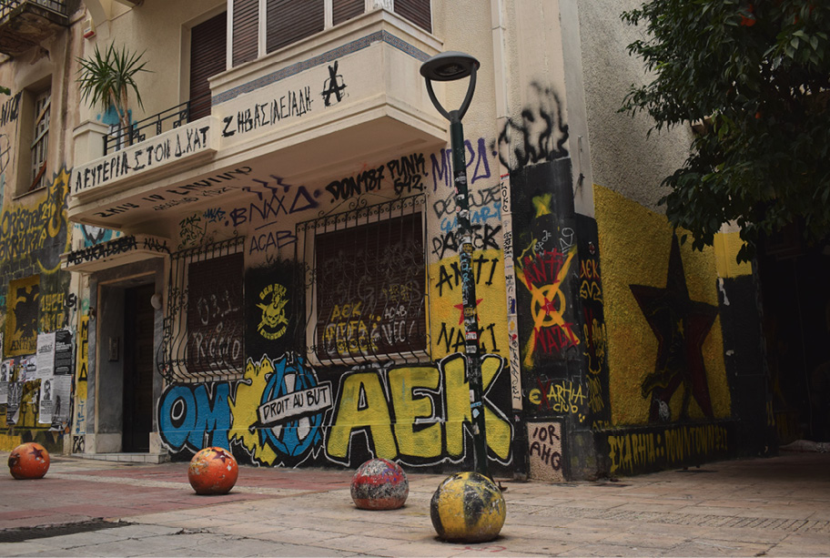 Elewacja budynku gęsto pokryta czarno-żółto-niebieskim graffiti poświęconym lokalnej drużynie piłkarskiej oraz hasłami i symbolami antyfaszystowskimi; na chodniku kolorowe betonowe kule.