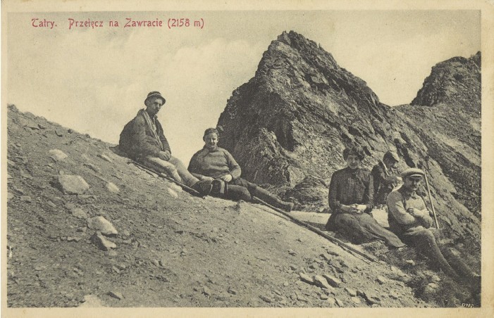 Czterech mężczyzn i kobieta siedzą na skałach na przełęczy. W tle góry. Kolor - sepia. 