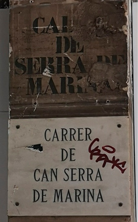 Black stencilled lettering on a wall, above a marble street sign mounted on the wall. 