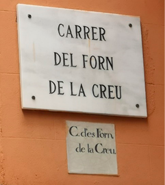 A marble street sign mounted on a wall, above a smaller ceramic sign set into the wall. 