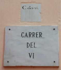 A marble street sign mounted on a wall, below a smaller ceramic sign set into the wall. 