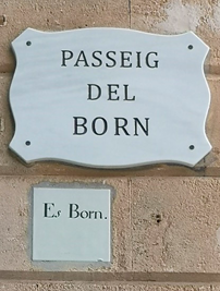 A marble street sign mounted on a wall, above a smaller ceramic sign set into the wall. 