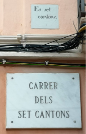 A marble street sign mounted on a wall, below a smaller ceramic sign set into the wall. 