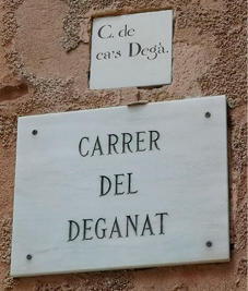A marble street sign mounted on a wall, below a smaller ceramic sign set into the wall. 