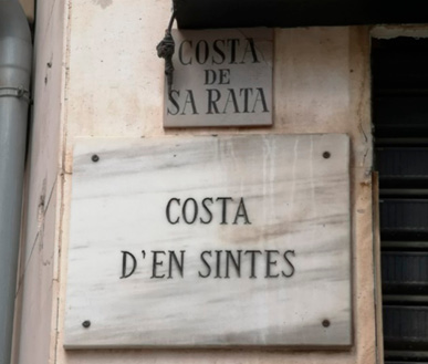 A marble street sign mounted on a wall, below a smaller marble sign mounted on the wall. 
