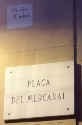 A marble street sign mounted on a wall, below a smaller ceramic sign set into the wall. 
