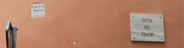 A marble street sign mounted on a wall, to the right of a smaller ceramic sign set into the wall. 