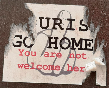 An anti-tourist sticker stuck on a wall, with torn edges. 