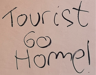 An anti-tourism message written on a wall in black marker pen. 