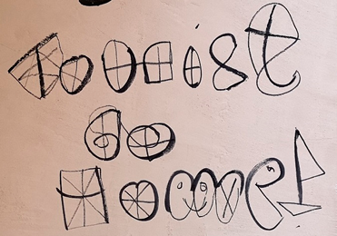 An anti-tourism message written on a wall in black marker pen, with improvised drawings over each letter, in a thinner black marker pen. 