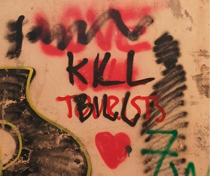 Graffiti on a wall in black and red spray paint. Different messages are written and effaced above, with a red heart below. 