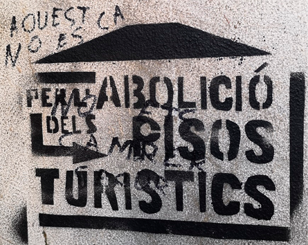 A black stencilled anti-tourism message, spray-painted on a wall. 