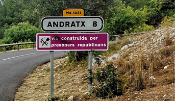 A road sign stating the distance to Andratx (8km), above a sign stating the road was built by Republican prisoners. 
