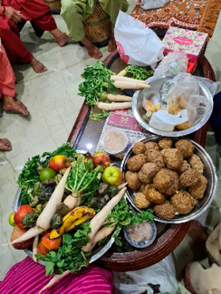 On the right, offerings for Dev Uthan Ekadashi displayed on a table, including radishes, fruits, green vegetables, and large, round sweets, surrounded by people preparing for the ritual.